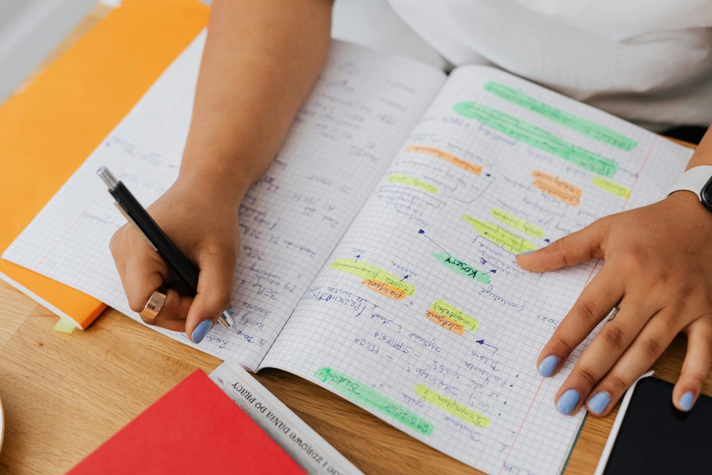 A photo of a young person writing maths equations in a square lined notebook.