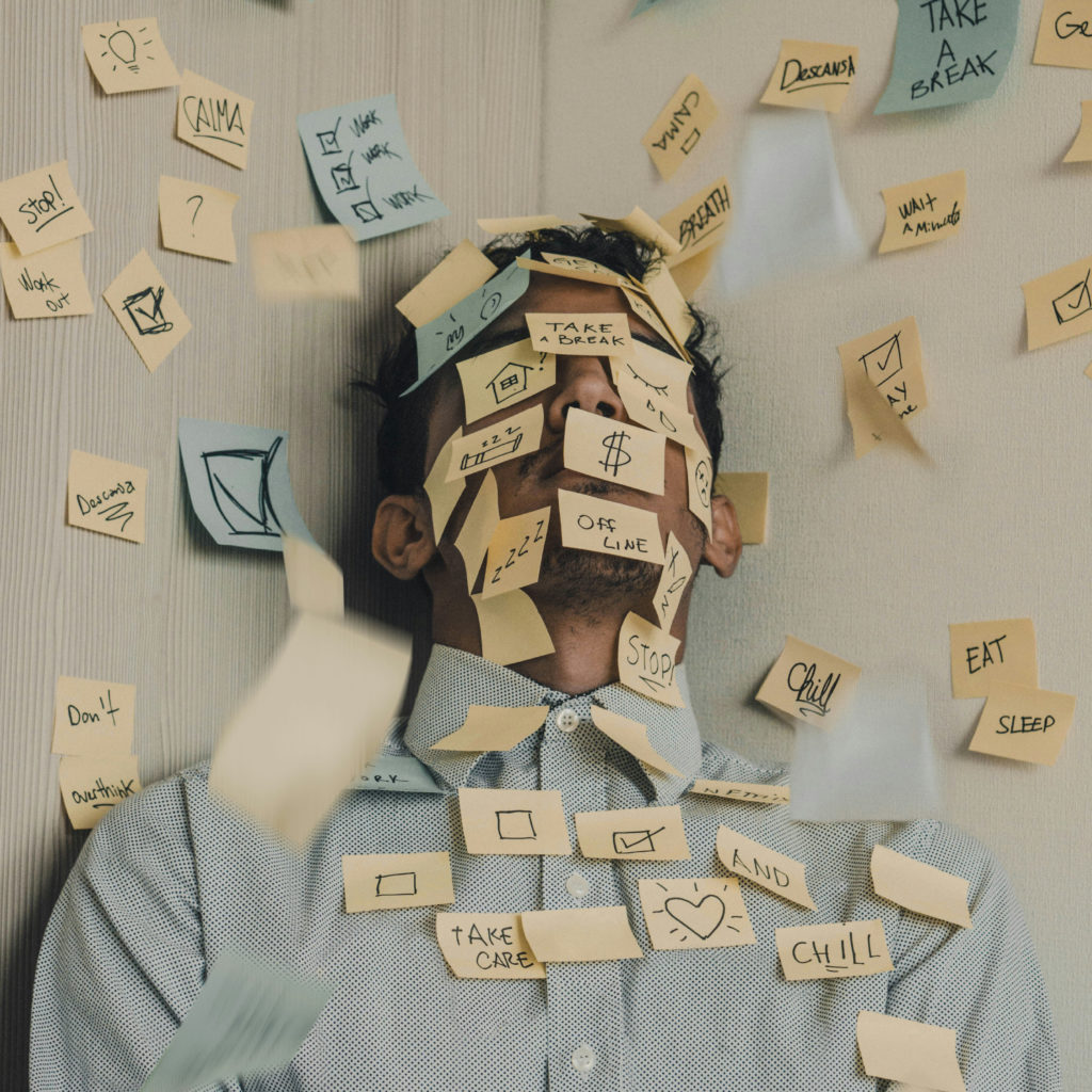A young man sits in a corner covered in different coloured post-it notes.