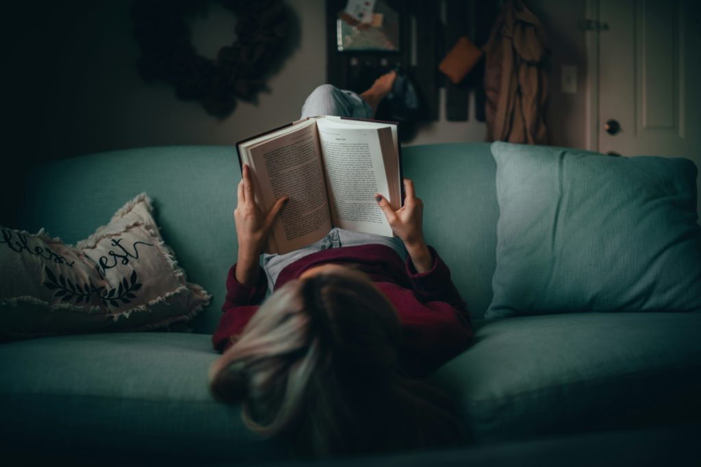 A young person laying back on a sofa reading